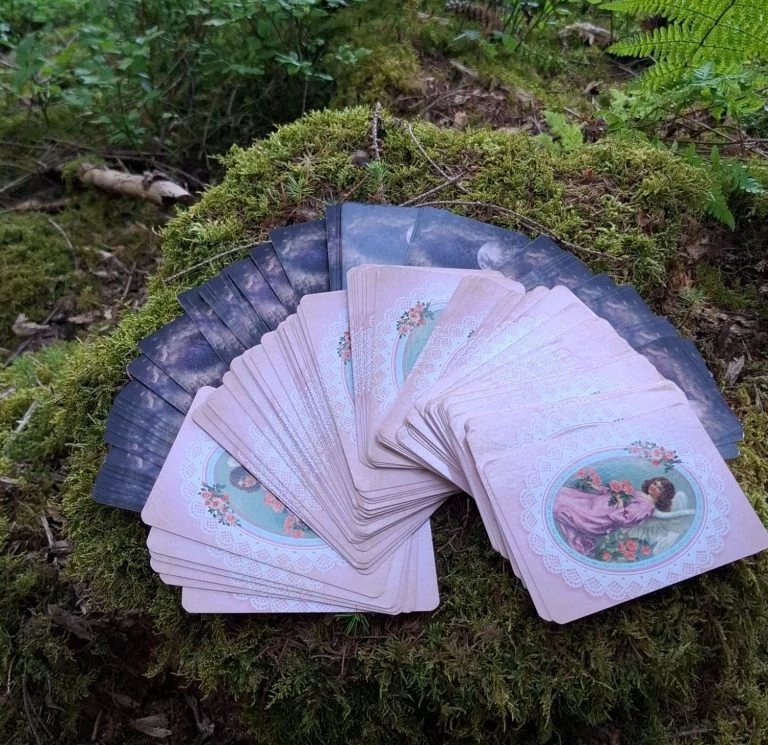 Aufgefächerte Orakel- und Tarotkarten auf einem moosbedeckten Waldboden